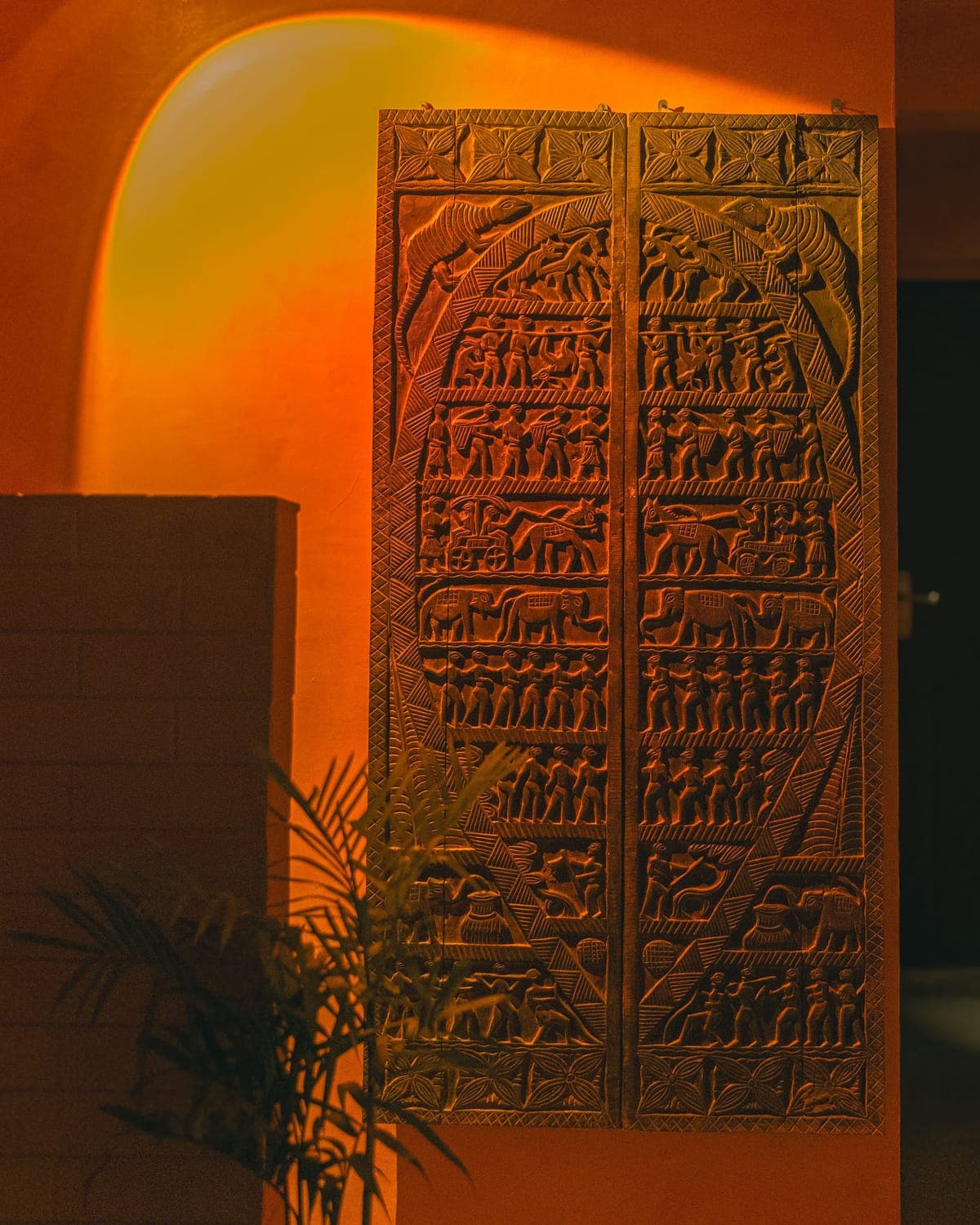 Carved wooden Mithila art panel illuminated by warm light at KohBar